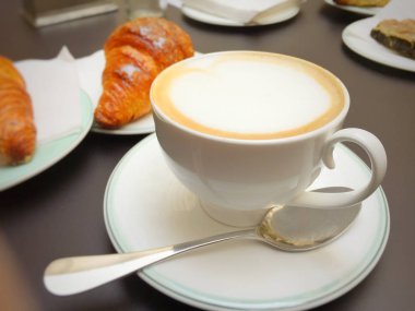 Kapuçino beyaz Kupası, kruvasan karanlık retro arka plan, seçici odak üzerinde. Kahvaltı konsepti