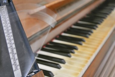 Antique metronome marks the rhythm of the music on an old wooden piano clipart