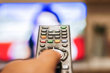 Bulanık bir televizyon ekranının önündeki kanalları değiştirmek için uzaktan kumanda düğmesine basan bir el