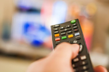 Bulanık bir televizyon ekranının önündeki kanalları değiştirmek için uzaktan kumanda düğmesine basan bir el