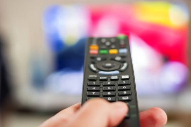 Bulanık bir televizyon ekranının önündeki kanalları değiştirmek için uzaktan kumanda düğmesine basan bir el