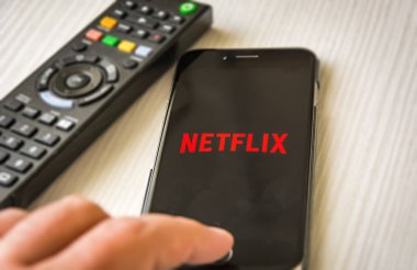 Roma, İtalya, 12 Ocak 2019; İnsan eli Netflix Tv Uzaktan kumanda ile arka planda içerik akışı izlemek için akıllı telefon kullanır