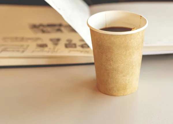 Café em papel reciclável vidro descartável com caderno aberto em fundo — Fotografia de Stock