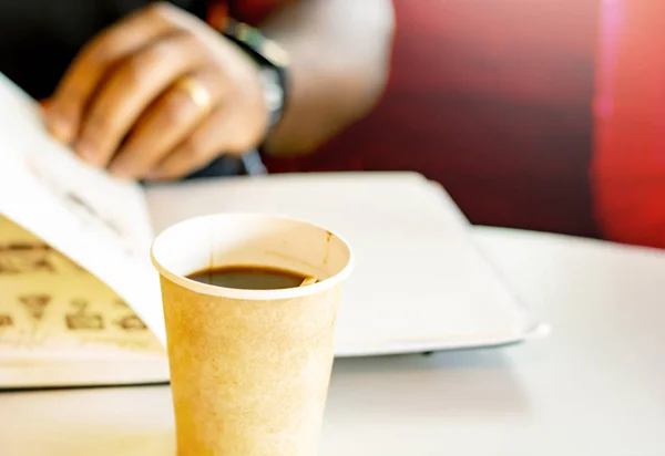 Ein Becher Kaffee mit einem schwarzen Mann, der ein Buch liest — Stockfoto