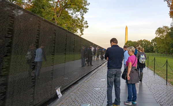 A couple of tourists contemplating the Vietnam Memorial Wall with the George Washington monument in the background — Stock Photo, Image