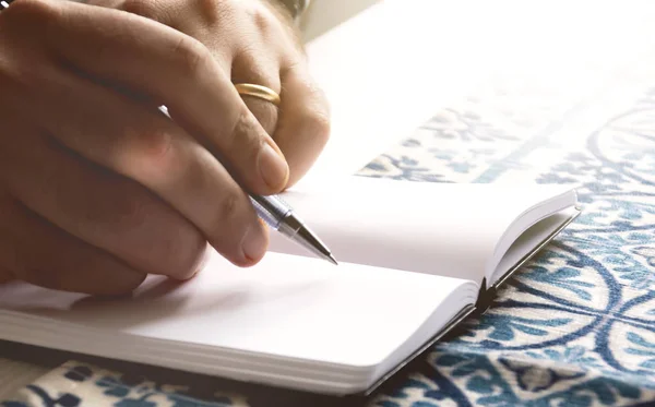 Mãos masculinas segurando uma caneta esferográfica para escrever nas páginas em branco de um caderno aberto . — Fotografia de Stock