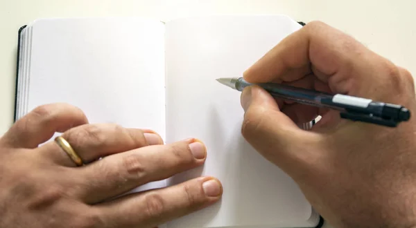 Mãos masculinas segurando uma caneta esferográfica para escrever nas páginas em branco de um caderno aberto . — Fotografia de Stock