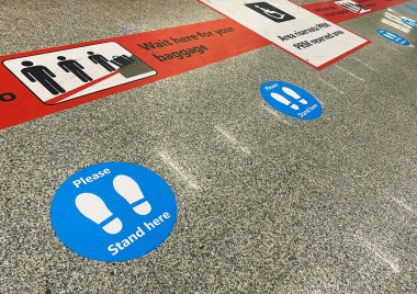 Havaalanındaki bagaj teslim kemerinin yanındaki yerde sosyal mesafeyi korumakla ilgili uyarılar var.