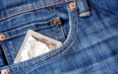 Bir kot pantolonun ön cebinden bir prezervatif fırlıyor. Cinsel yolla bulaşan hastalıkların önlenmesi. Güvenli seks.