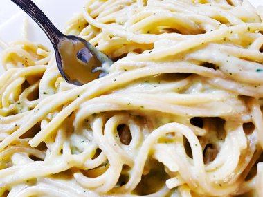 Kremalı spagetti tabağında bir çatal. İtalyan yemeği. Karbonhidratlar ve kremalı tarifler.
