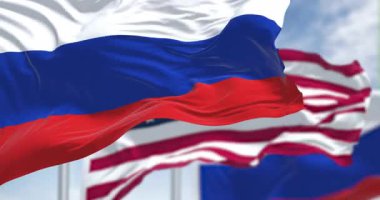 Parlak bir günde, diplomasi, kimlik ve uluslararası ilişkileri sembolize eden üç boyutlu Rus ve Amerikan bayrakları dalgalanıyor. Kusursuz 3 boyutlu animasyon. Yavaş çekim döngüsü. Seçici odak