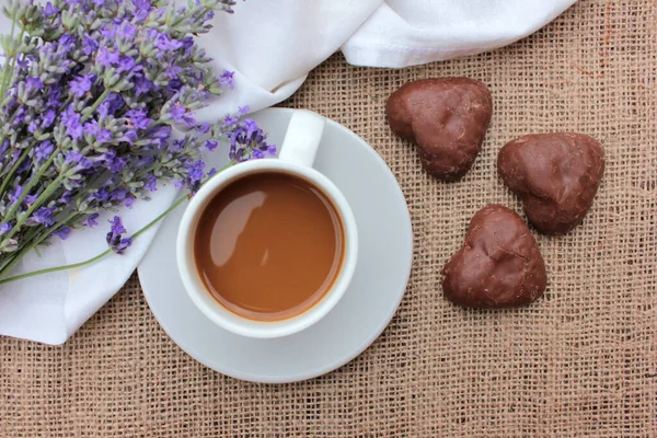 Cup of coffee with lavender flowers and chocolate heart shaped cookies on burlap texture. Top view