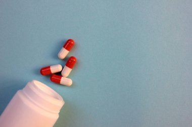 Beyaz ilaç şişesi, mavi arka planda kırmızı ve beyaz haplar. Üst görünüm, kopyalama alanı, seçici odak