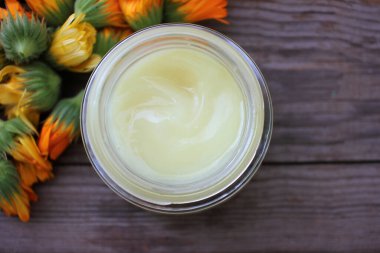 Takvim çiçekleri ve cam kavanozdaki diy yüz kremi ahşap masa zemininde fotokopi alanı ile. Şifalı bitkilerle ev yapımı organik kozmetik ürünler..