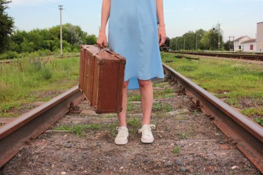 Demiryolunda mavi elbiseli genç bir kadın ve eski bir bavul.