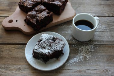 Kesme tahtasında kirazlı brownie. Ahşap masa arkasında kahve bulunan el yapımı çikolatalı kekin yakın çekimi. Üst görünüm, alanı kopyala