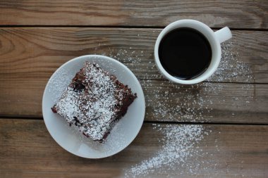 Ahşap masa arkasında el yapımı çikolatalı kek olan bir fincan kahve. Beyaz tabakta kirazlı brownie. Üst görünüm, alanı kopyala
