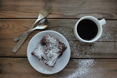 Ahşap masa arkasında el yapımı çikolatalı kek olan bir fincan kahve. Beyaz tabakta kirazlı brownie. Üst görünüm, alanı kopyala