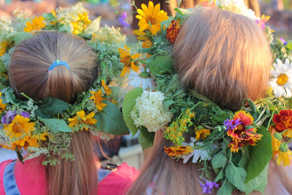 Two girls' heads in crowns of wildflowers, closeup, back view. Ukrainian flower wreath for Ivana Kupala at Midsummer Fest