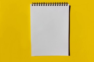 Boş beyaz defter sayfası, parlak sarı arkaplanlı ve kopyalama alanı olan bir spiralde. Üst görünüm, alanı kopyala.