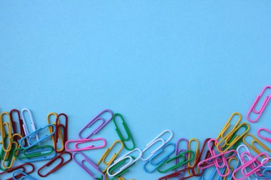 Mavi arkaplanda fotokopi alanı olan renkli ataçların üst görünümü. Okula ya da ofis konseptine dönmek