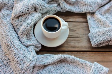 Kırsal ahşap arka planda bir fincan kahve ve açık gri örgü süveter. Sıcak sonbahar ya da kış konsepti. Üst görünüm, alanı kopyala