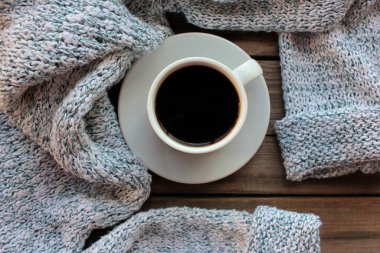 Kırsal ahşap arka planda bir fincan kahve ve açık gri örgü süveter. Sıcak sonbahar ya da kış konsepti. Üst görünüm, alanı kopyala