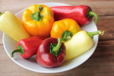 Beyaz tabakta kırmızı, turuncu ve sarı dolmalık biber. Tahta bir masada taze sebzeler. Üst görünüm, alanı kopyala