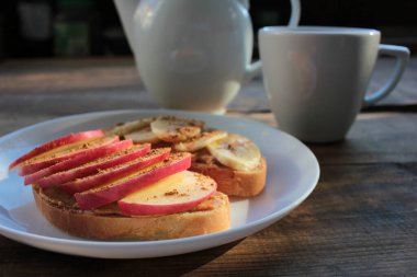 Fıstık ezmeli, muzlu, tarçınlı, tarçınlı ve çayla kahvaltı. Fıstık ezmeli ekmek dilimleri ve tabakta taze meyveler. Çocuklar için sağlıklı atıştırmalıklar. 