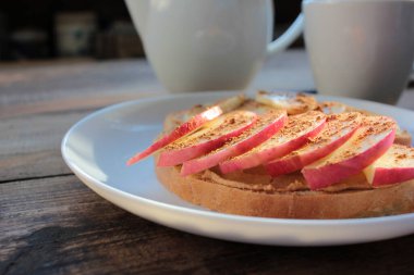 Fıstık ezmeli, muzlu, tarçınlı, tarçınlı ve çayla kahvaltı. Fıstık ezmeli ekmek dilimleri ve tabakta taze meyveler. Çocuklar için sağlıklı atıştırmalıklar. 