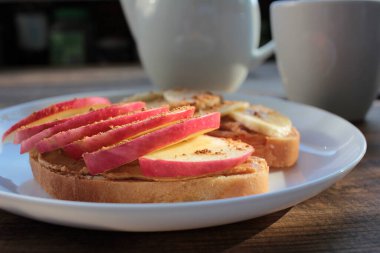 Fıstık ezmeli, muzlu, tarçınlı, tarçınlı ve çayla kahvaltı. Fıstık ezmeli ekmek dilimleri ve tabakta taze meyveler. Çocuklar için sağlıklı atıştırmalıklar. 