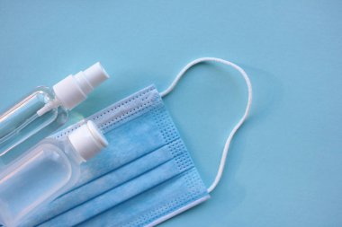 Tıbbi yüz maskesi ve el dezenfektanı şişeleri mavi arka planda fotokopi alanı ile birlikte. Salgın koruma kiti.