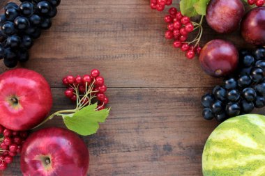 Üzümlerden, karpuzlardan, eriklerden, kırmızı viburnum üzümlerinden ve ahşap masadaki elmalardan oluşan doğal yapı. Sonbahar hasat geçmişi. Üst görünüm, alanı kopyala