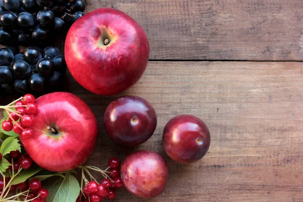 Red apples, grapes, plums, and viburnum berries on wooden table. Autumn harvest background. Top view, copy space. Fruits and berries on the table