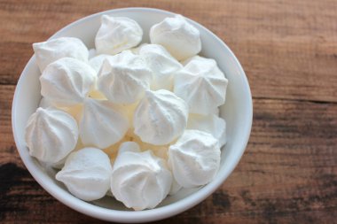 Beyaz bir tabakta kremalı pastaya yakın plan. Ahşap masa arkaplanındaki şekerlemeler, seçici odak