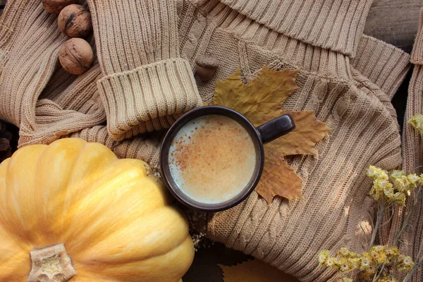 Cup of pumpkin latte with cinnamon, sweater, pumpkin, and fall leaves. Cozy autumn concept. Autumn composition. Selective focus