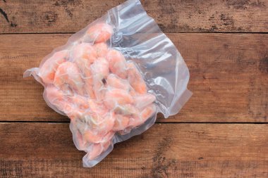Haşlanmış ve donmuş karidesler vakumlu şeffaf plastik ambalaj poşetinde ahşap arka planda..
