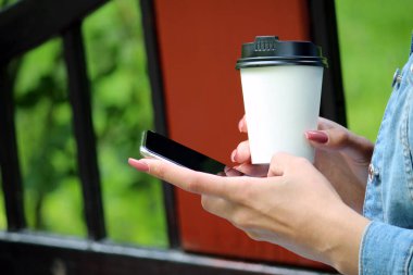 Elinde telefon ekranı menüsü ve kahve kapuçinosu olan çıplak manikürlü iş kadını kız öğrenci.