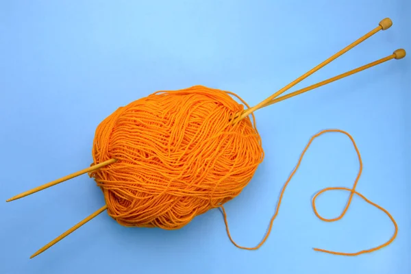 Mavi arka planda örgü iğneleriyle turuncu iplik örüyorlar.