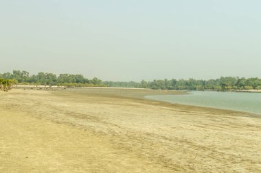Golden hour light illuminates a serene tidal flat, with patterned wet sand, colorful skies, and distant figures adding scale and a peaceful coastal or beach vibe