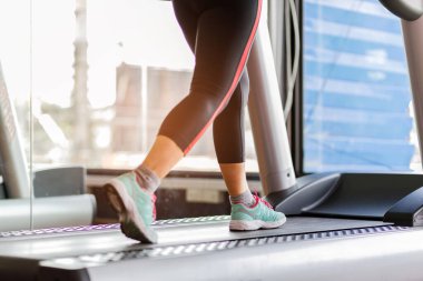 Koşu bandında koşan ayak ayakkabısı fitness kızı spor salonunda kaslı bacakları olan şişman kadın. Sağlıklı yaşam kavramı.