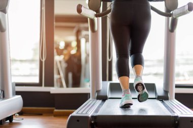 Koşu bandında koşan ayak ayakkabısı fitness kızı spor salonunda kaslı bacakları olan şişman kadın. Sağlıklı yaşam kavramı.