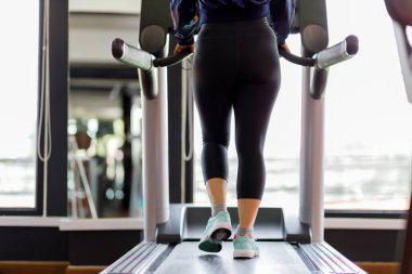 Koşu bandında koşan ayak ayakkabısı fitness kızı spor salonunda kaslı bacakları olan şişman kadın. Sağlıklı yaşam kavramı.