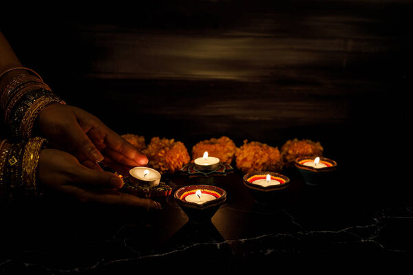 Happy Diwali - Woman hands with henna holding lit candle isolated on dark background. Clay Diya lamps lit during Dipavali, Hindu festival of lights celebration. Copy space for text.