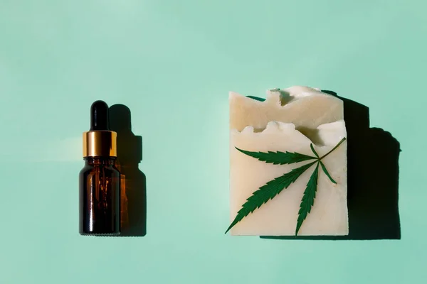 Cannabis oil with a dropper of hemp oil and handmade soap with a beautiful hemp leaf in the sun on a light green background. An environmentally friendly product useful for health. Top view, close-up.