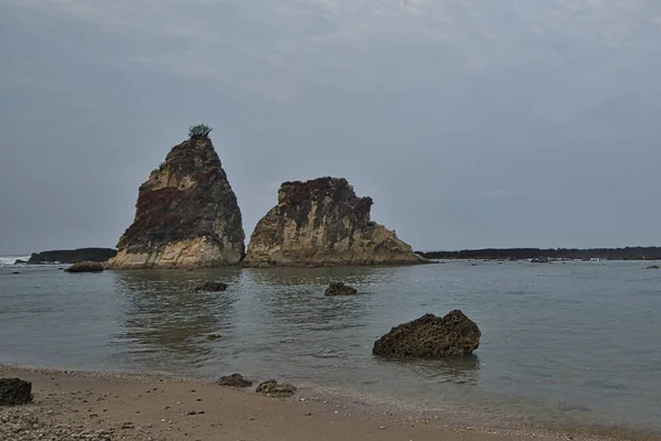 natural landscape of the beach at noon with large rocks forming clusters as if challenging the waves, against the cloudy blue sky, location on Tanjung Layar Sawarna Beach West Java Indonesia.