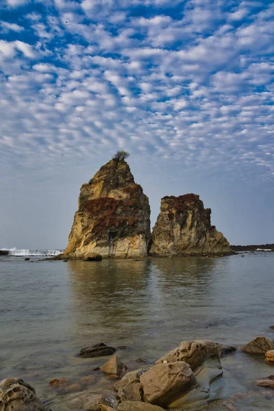 natural landscape of the beach at noon with large rocks forming clusters as if challenging the waves, against the cloudy blue sky, location on Tanjung Layar Sawarna Beach West Java Indonesia