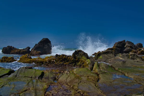 natural landscape of the beach at noon with large rocks forming clusters as if challenging the waves, against the cloudy blue sky, location in Sawarna Beach West Java Indonesia