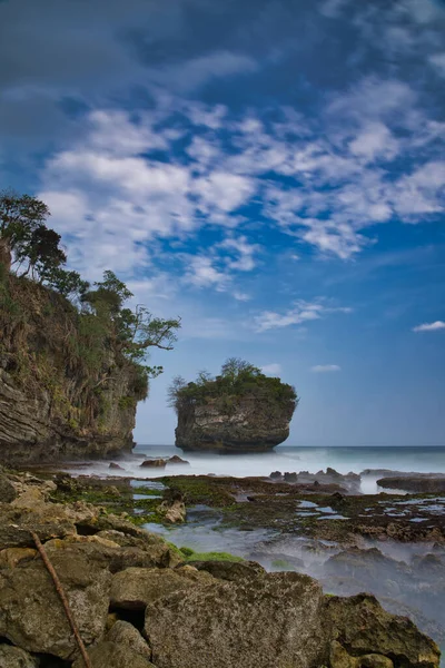 natural landscape of the beach at noon with large rocks forming clusters as if challenging the waves, against the cloudy blue sky, location in Sawarna Beach West Java Indonesia