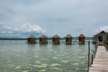 Seram, Maluku Endonezya 'nın batısında, mavi ve bulutlu gökyüzüne karşı uzanan çok sayıda geleneksel evden oluşan denizin ortasındaki tatil köyü manzarası